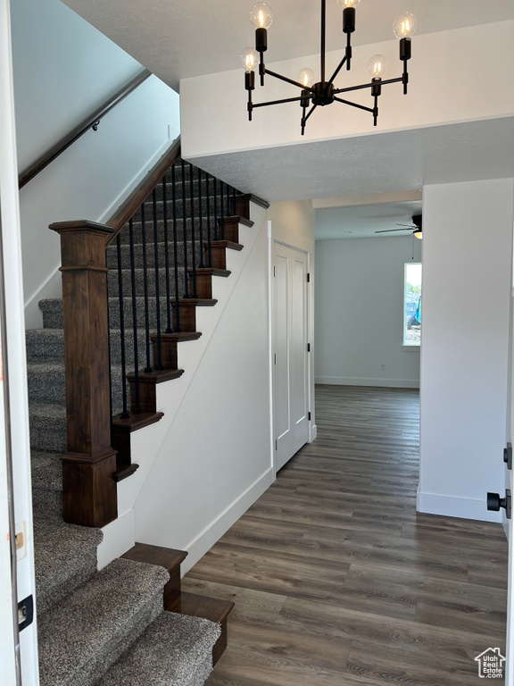 Staircase featuring ceiling fan with notable chandelier and dark wood-type flooring