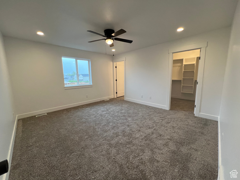 Unfurnished bedroom with a spacious closet, a closet, ceiling fan, and dark carpet