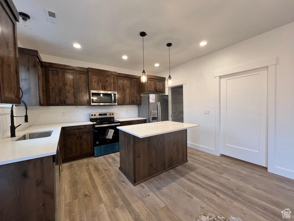 Kitchen featuring appliances with stainless steel finishes, pendant lighting, a kitchen island, and light hardwood / wood-style floors