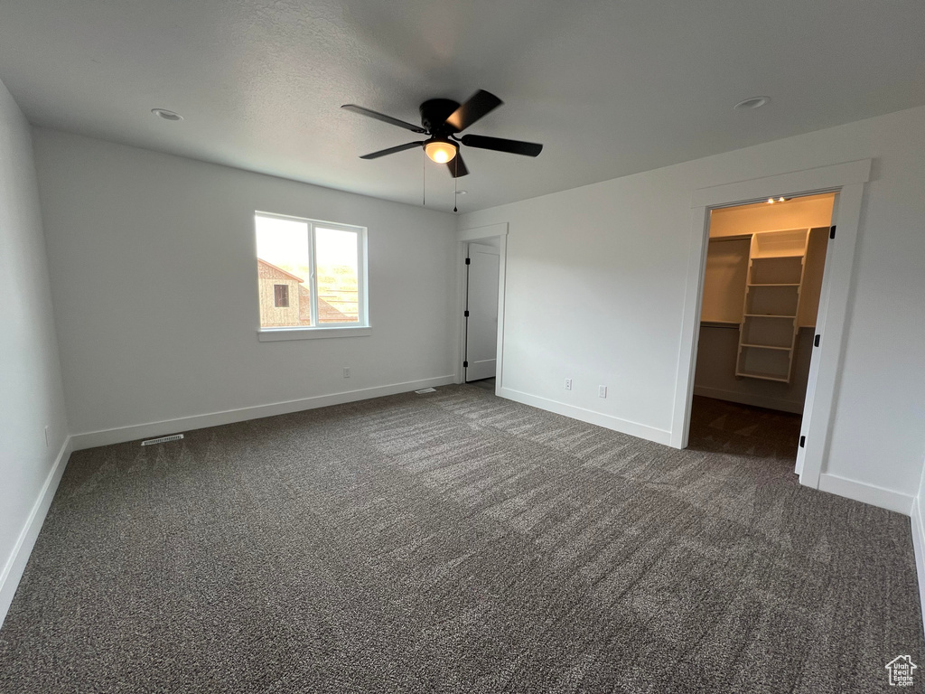 Unfurnished bedroom featuring a spacious closet, a closet, ceiling fan, and dark colored carpet