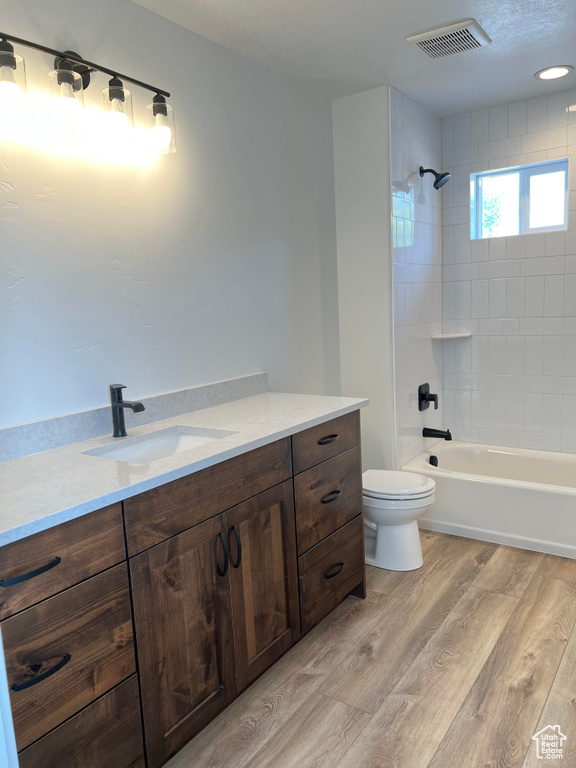 Full bathroom with wood-type flooring, tiled shower / bath, vanity, and toilet