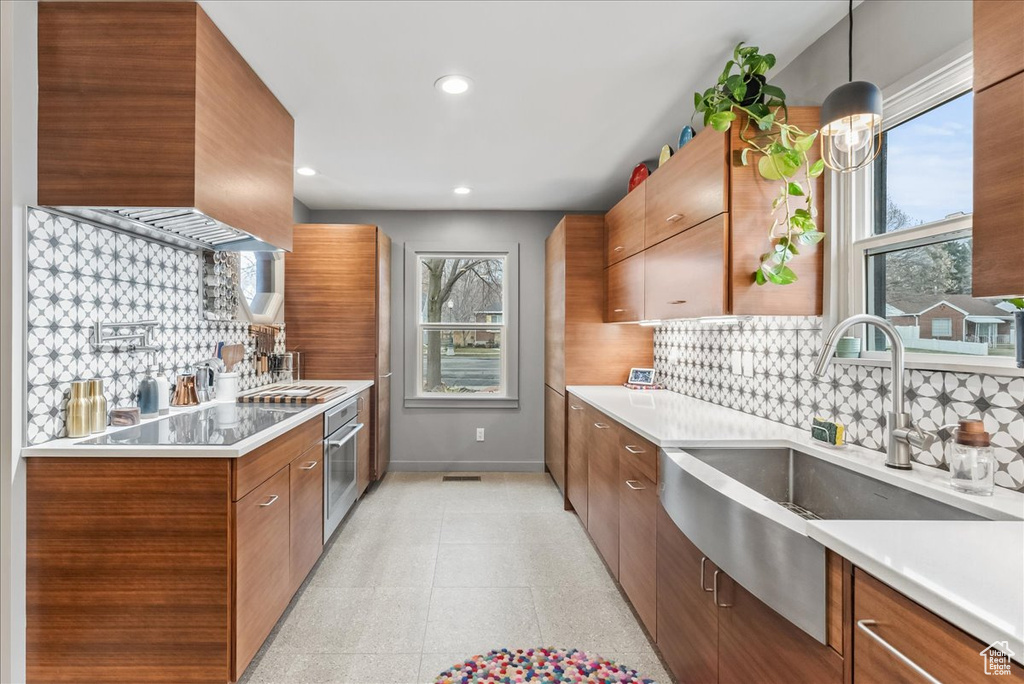 Kitchen featuring stainless steel oven, backsplash, hanging light fixtures, sink, and light tile floors