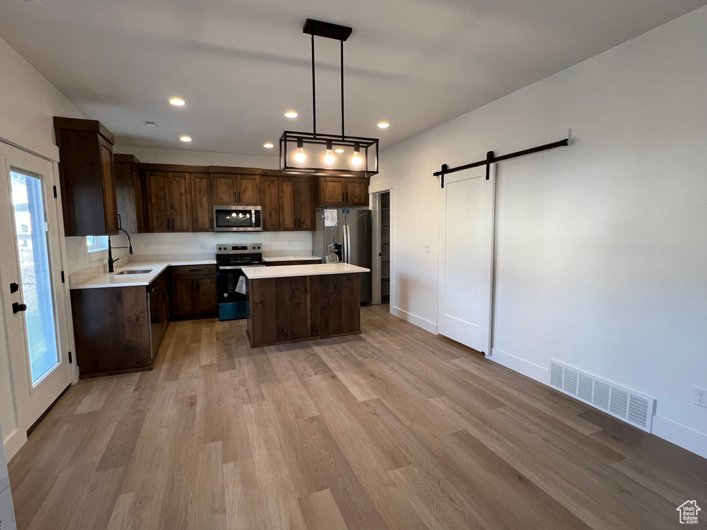 Kitchen featuring a barn door, appliances with stainless steel finishes, light hardwood / wood-style flooring, a kitchen island, and decorative light fixtures