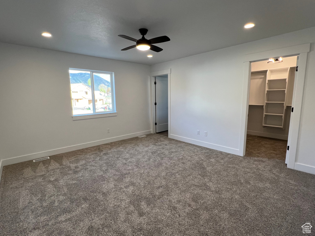 Unfurnished bedroom with a walk in closet, ceiling fan, and dark colored carpet