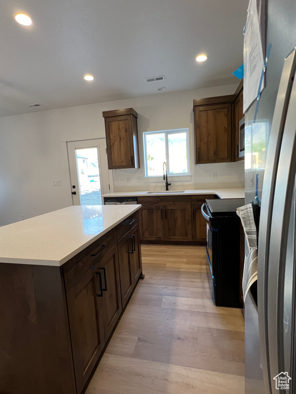 Kitchen with a kitchen island, light hardwood / wood-style flooring, electric stove, stainless steel refrigerator, and sink