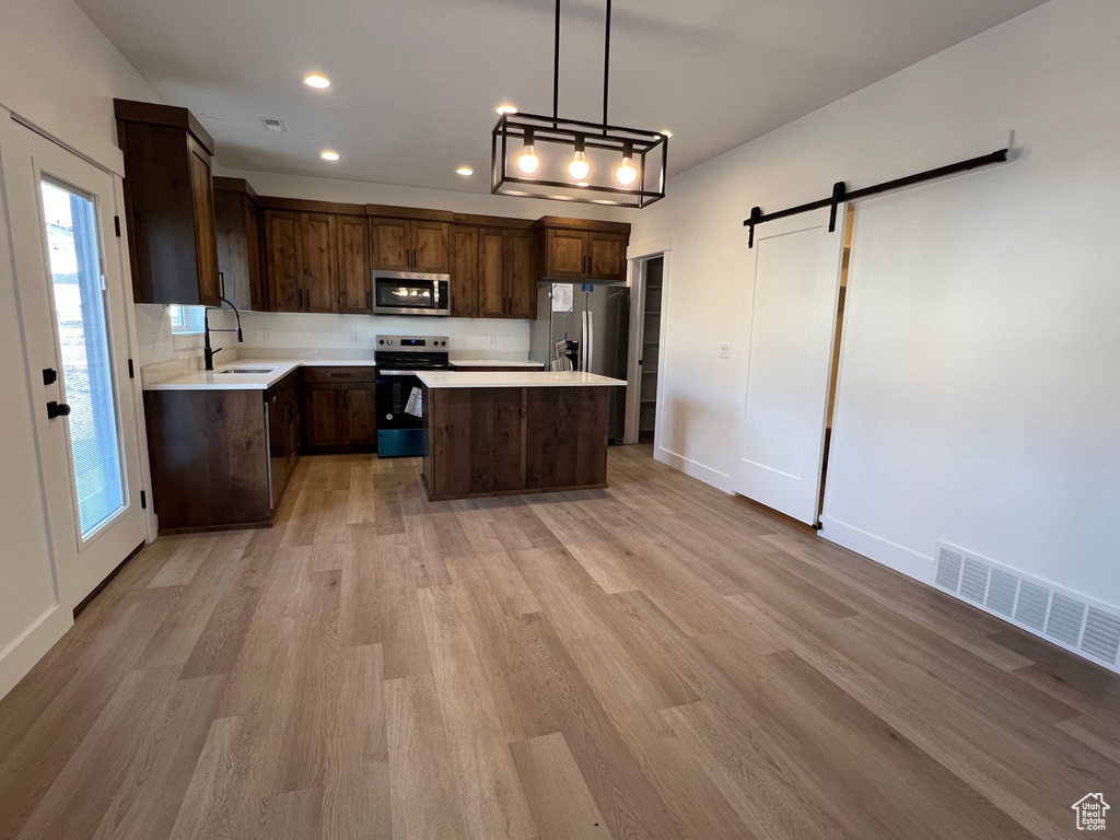 Kitchen featuring decorative light fixtures, a kitchen island, a barn door, stainless steel appliances, and light wood-type flooring