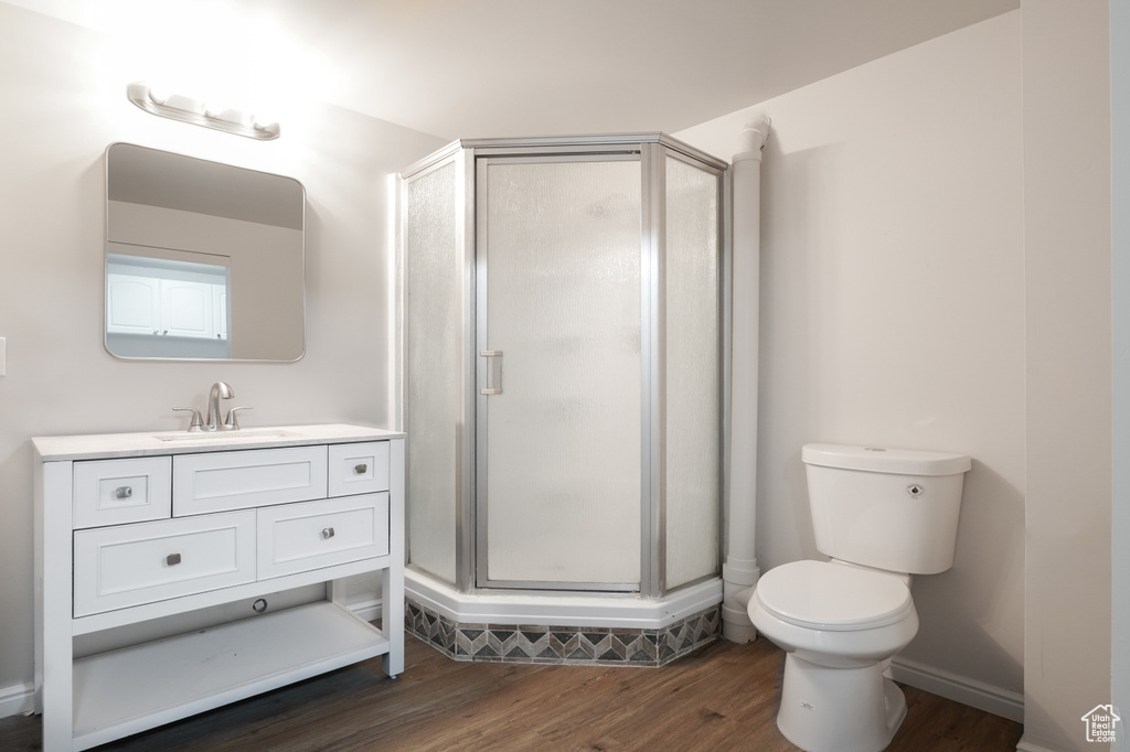 Bathroom with wood-type flooring, a shower with door, toilet, and vanity