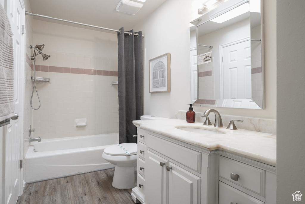 Full bathroom with oversized vanity, shower / bath combination with curtain, toilet, and hardwood / wood-style floors