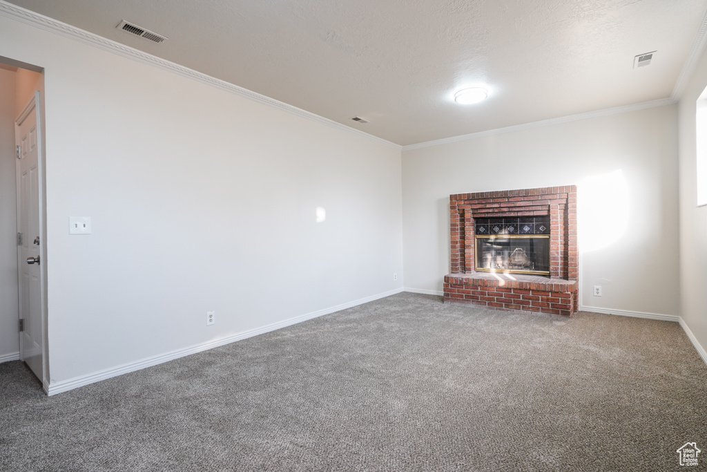 Unfurnished living room with a brick fireplace, ornamental molding, and dark colored carpet