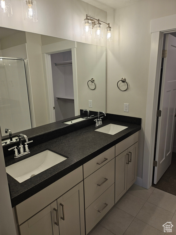 Bathroom featuring double sink, tile flooring, large vanity, and a shower with shower door