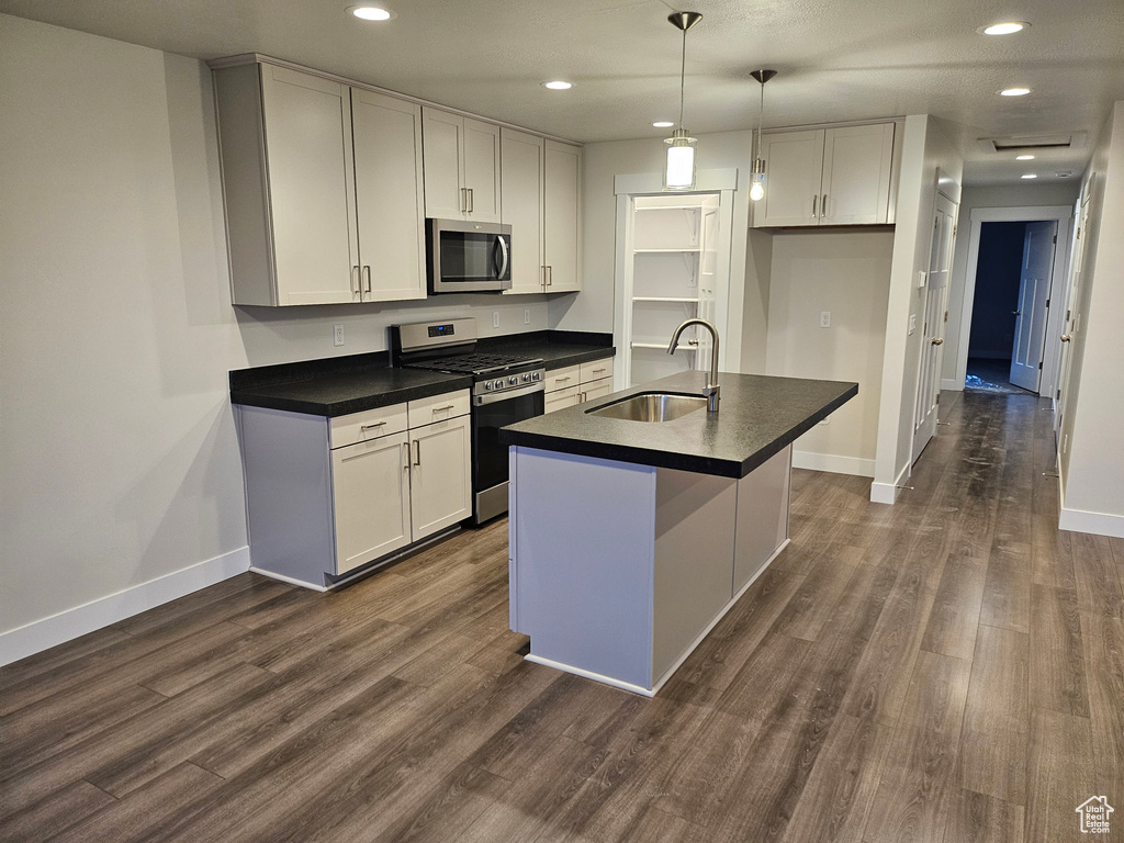 Kitchen featuring dark hardwood / wood-style flooring, sink, decorative light fixtures, white cabinetry, and stainless steel appliances