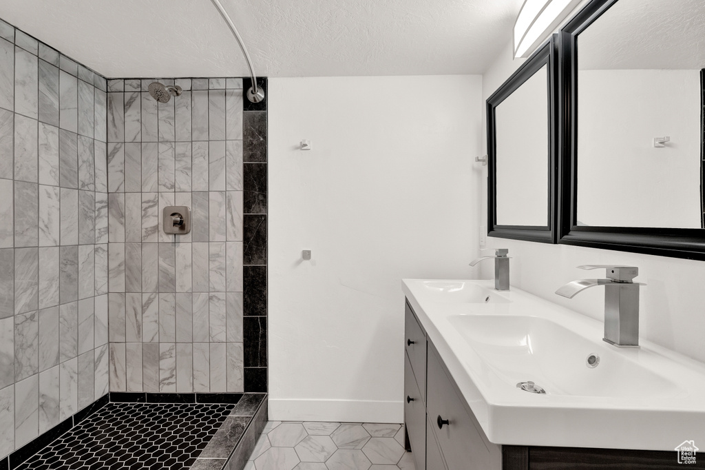 Bathroom with dual bowl vanity, tile flooring, and tiled shower