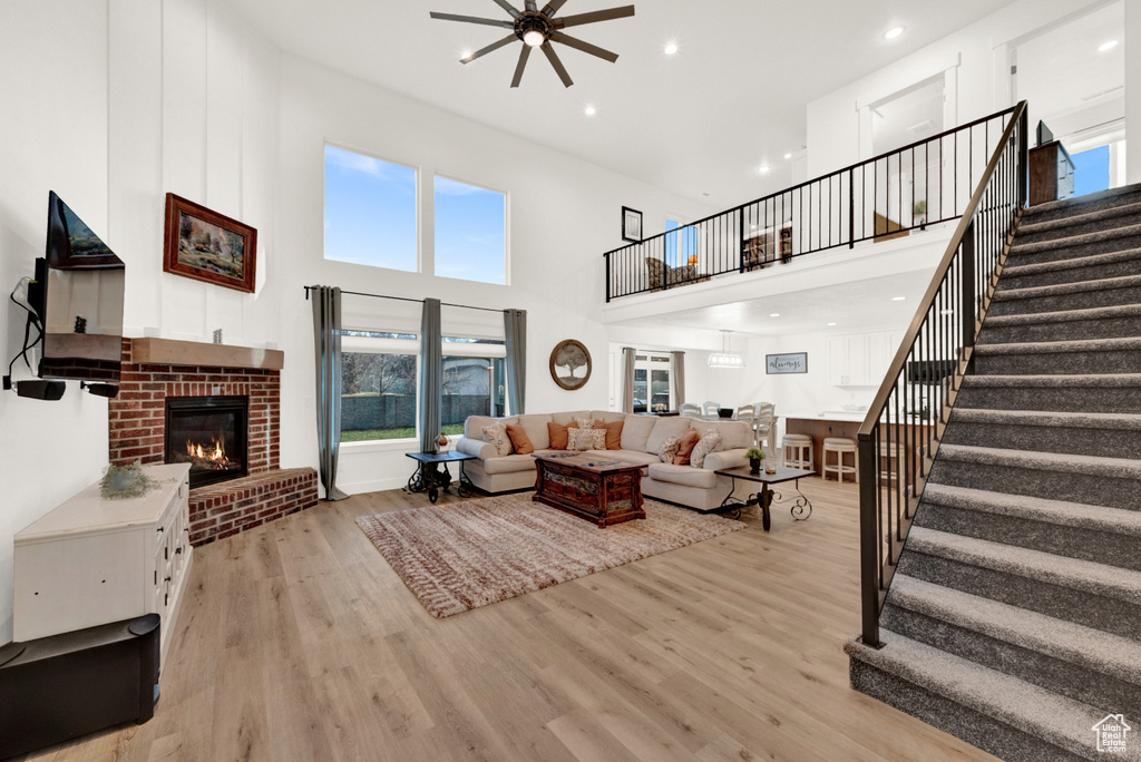 Living room with a high ceiling, light wood-type flooring, ceiling fan, and a brick fireplace