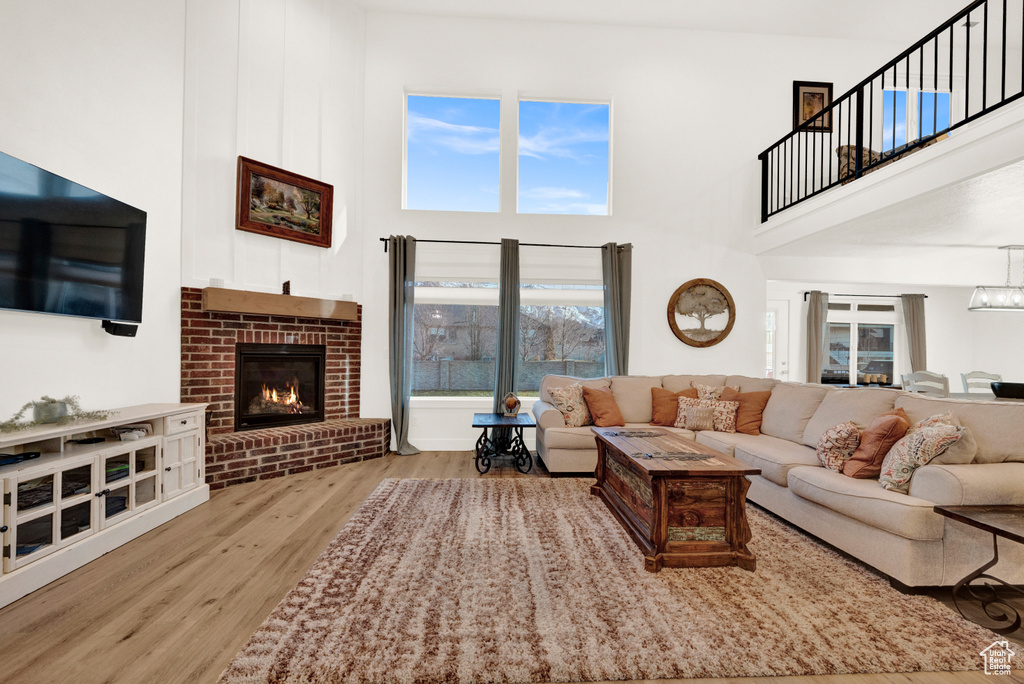 Living room featuring a notable chandelier, light wood-type flooring, a high ceiling, and a brick fireplace