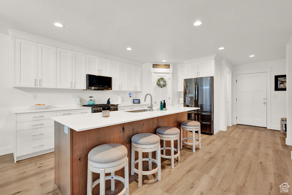 Kitchen featuring appliances with stainless steel finishes, a center island with sink, a breakfast bar, and light hardwood / wood-style flooring