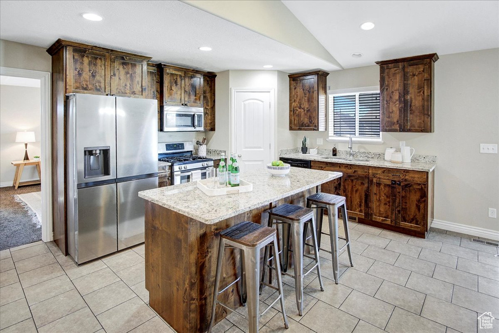 Kitchen with light tile floors, a kitchen island, stainless steel appliances, and light stone counters