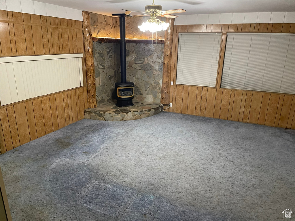 Unfurnished living room with wood walls, ceiling fan, a wood stove, and carpet