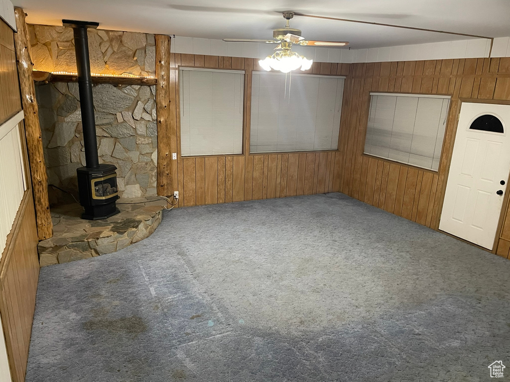 Unfurnished living room featuring wood walls, ceiling fan, a wood stove, and carpet flooring