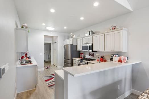 Kitchen with white cabinetry, appliances with stainless steel finishes, light hardwood / wood-style floors, and kitchen peninsula