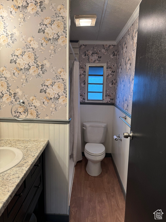 Bathroom with a textured ceiling, vanity, crown molding, hardwood / wood-style flooring, and toilet