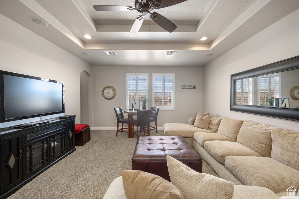 Carpeted living room with plenty of natural light, ceiling fan, and a tray ceiling