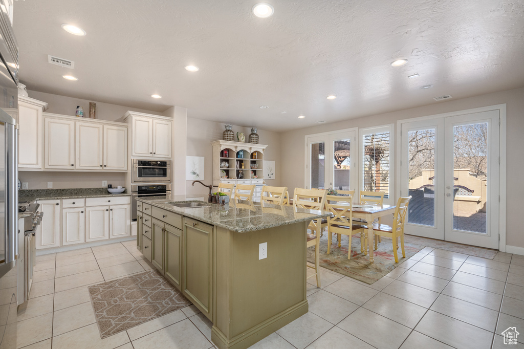 Kitchen with light tile floors, white cabinetry, a center island with sink, and light stone countertops