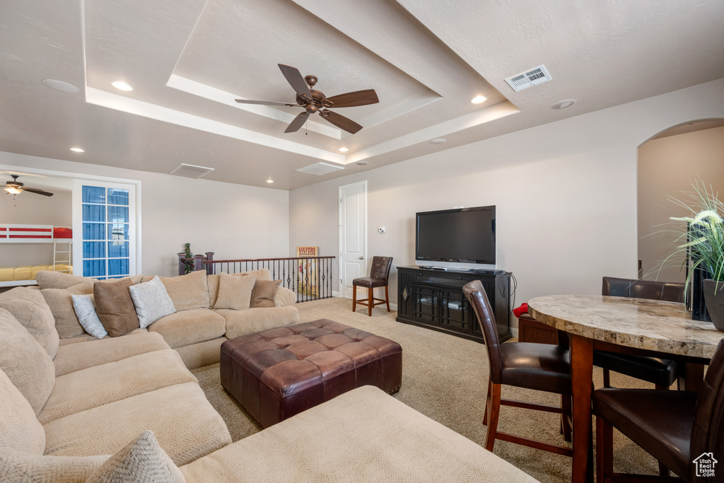 Carpeted living room with ceiling fan and a raised ceiling