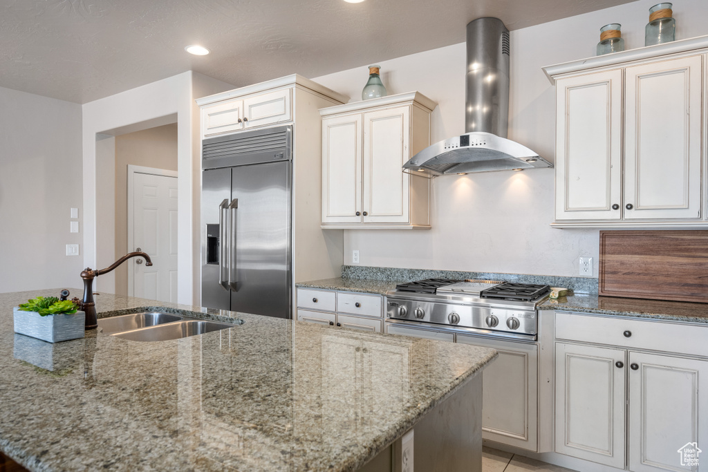 Kitchen featuring sink, stainless steel appliances, wall chimney range hood, and light stone counters