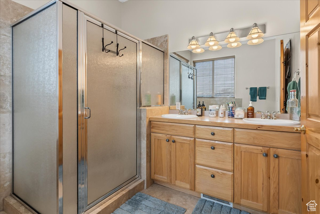 Bathroom featuring dual sinks, a shower with door, and vanity with extensive cabinet space