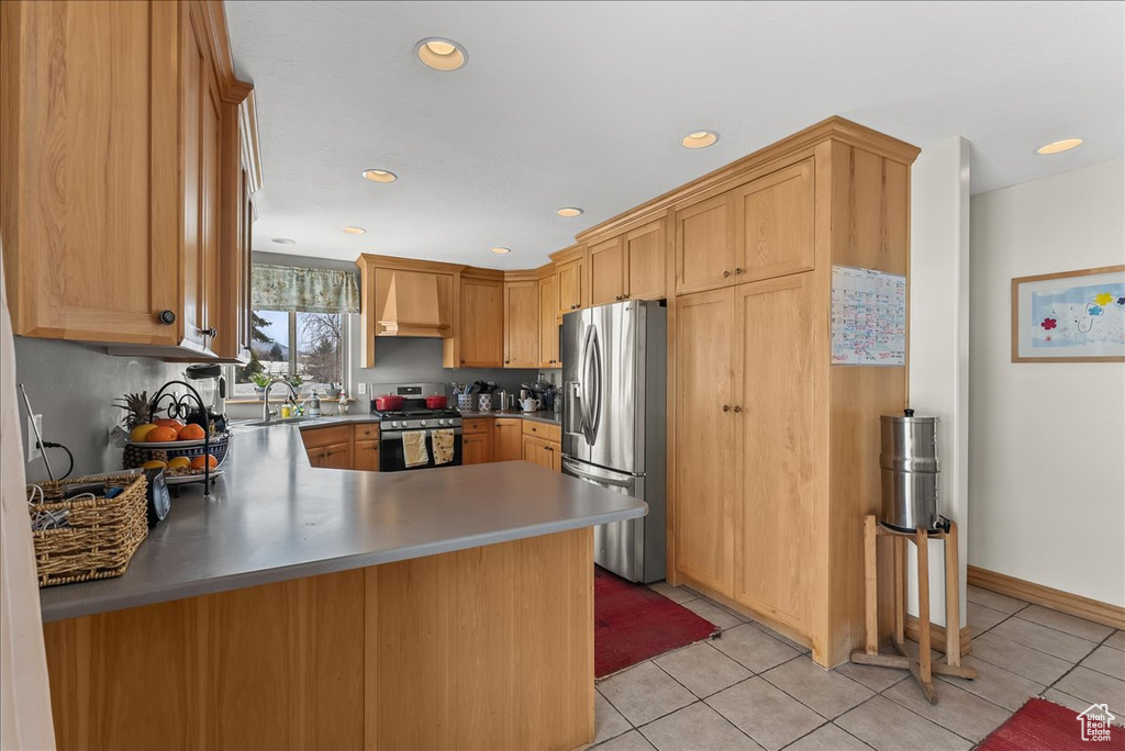 Kitchen with sink, premium range hood, light tile floors, kitchen peninsula, and appliances with stainless steel finishes