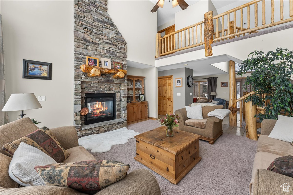 Living room with ceiling fan, a towering ceiling, light carpet, and a stone fireplace