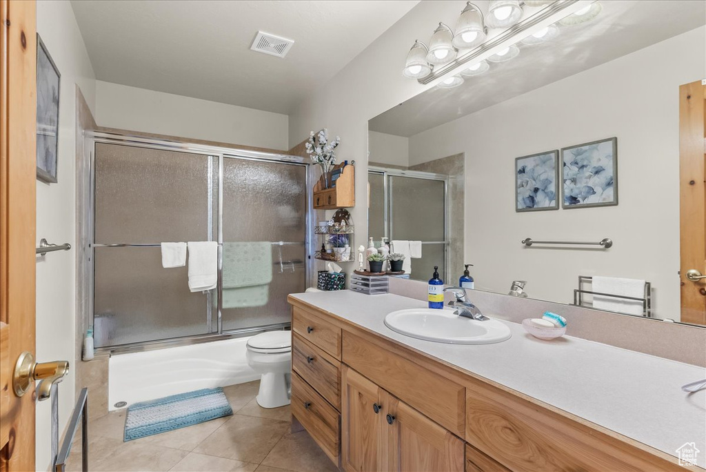 Full bathroom with tile floors, bath / shower combo with glass door, toilet, and large vanity