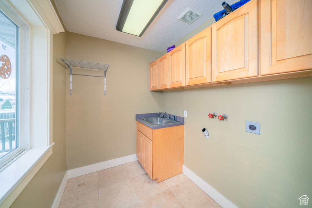 Clothes washing area with sink, cabinets, light tile floors, and electric dryer hookup