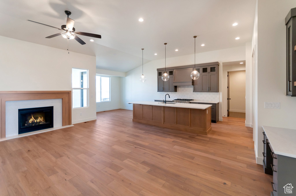 Kitchen featuring sink, tasteful backsplash, light hardwood / wood-style floors, a center island with sink, and ceiling fan