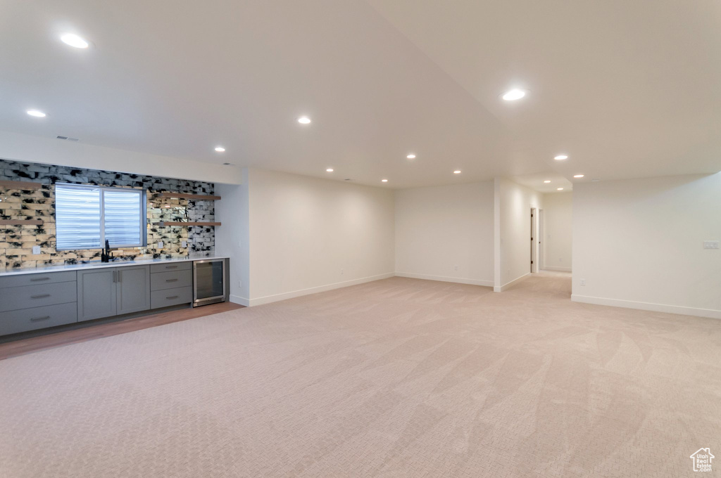 Basement with wine cooler, light colored carpet, and sink