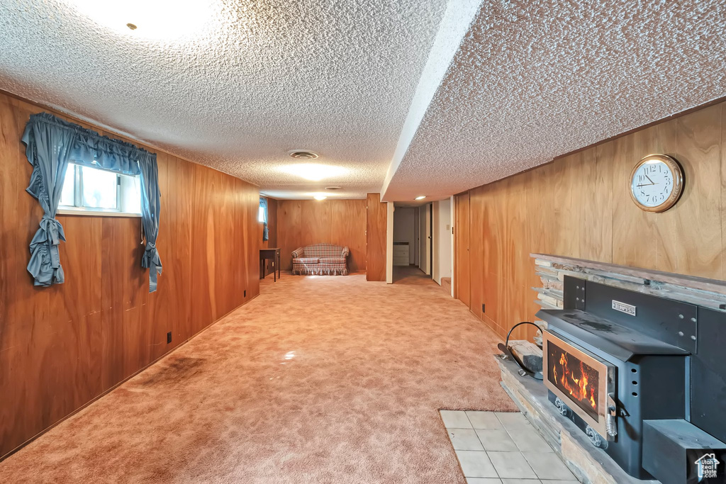 Basement with wood walls, light colored carpet, a textured ceiling, and a fireplace