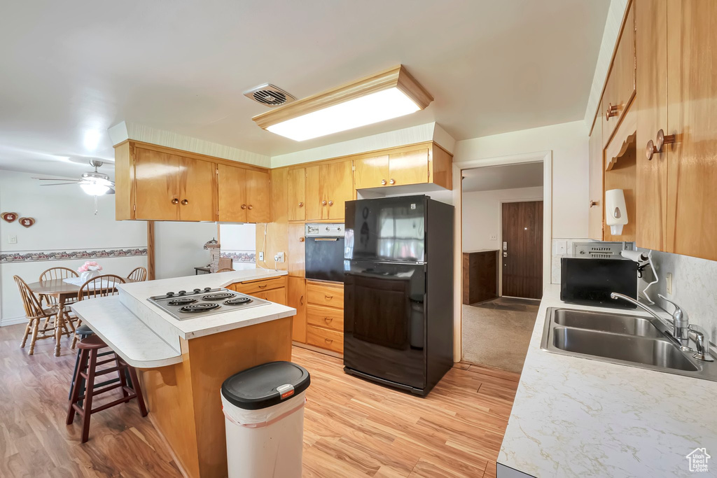 Kitchen with black refrigerator, a breakfast bar, light hardwood / wood-style flooring, sink, and ceiling fan