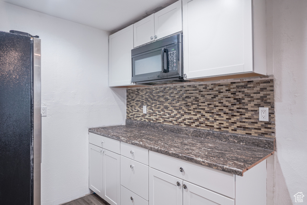 Kitchen featuring tasteful backsplash, stainless steel fridge, white cabinets, and dark stone countertops