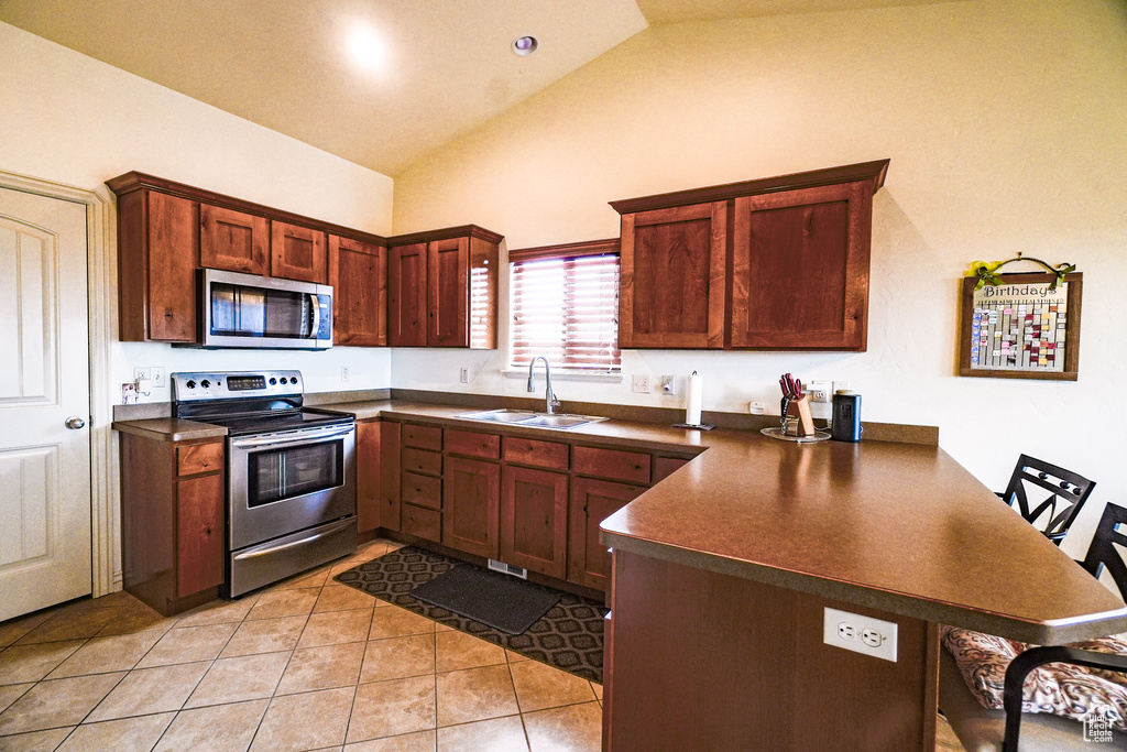 Kitchen with light tile flooring, vaulted ceiling, stainless steel appliances, and kitchen peninsula
