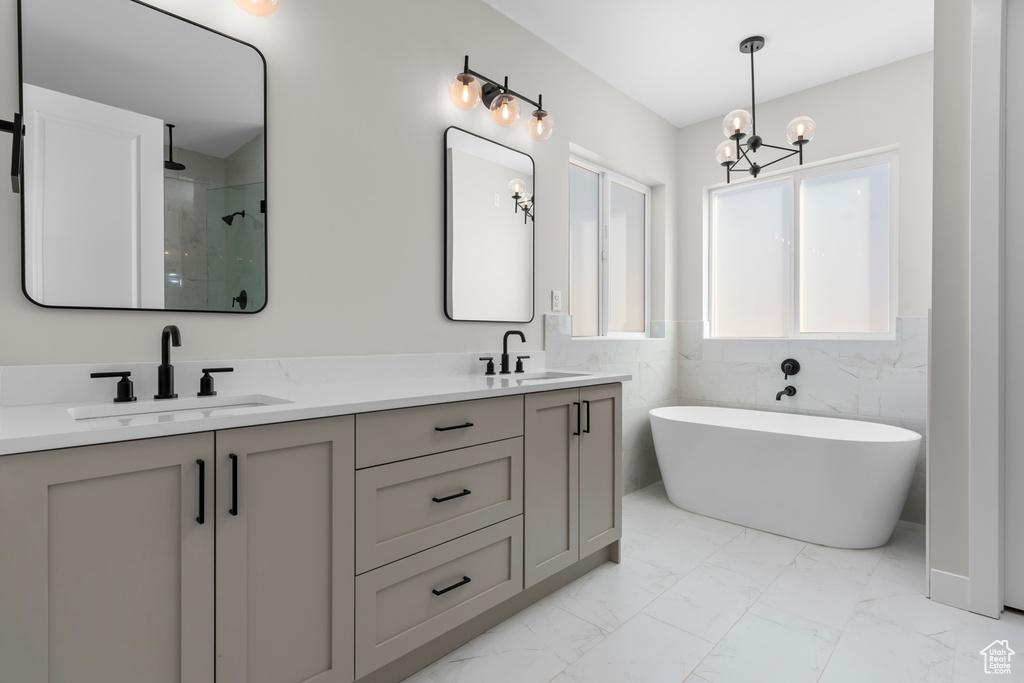 Bathroom with double sink vanity, tile walls, walk in shower, an inviting chandelier, and tile flooring