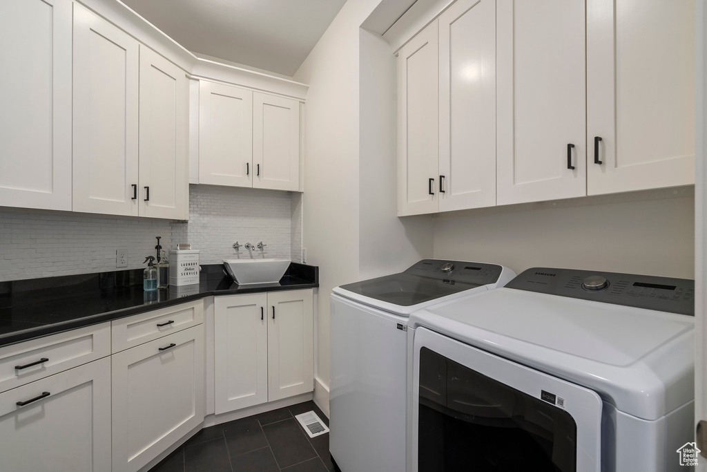 Laundry room featuring sink, cabinets, dark tile flooring, and washer and clothes dryer