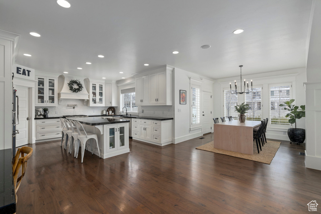 Kitchen with a breakfast bar, dark hardwood / wood-style floors, white cabinets, a notable chandelier, and backsplash