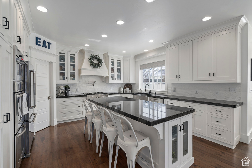 Kitchen featuring a breakfast bar area, a center island, white cabinetry, dark hardwood / wood-style flooring, and premium range hood