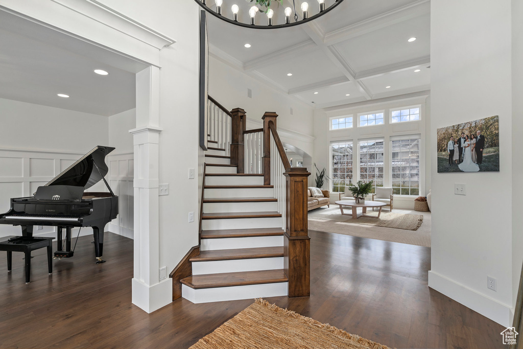Stairs with coffered ceiling, dark wood-type flooring, decorative columns, and a chandelier