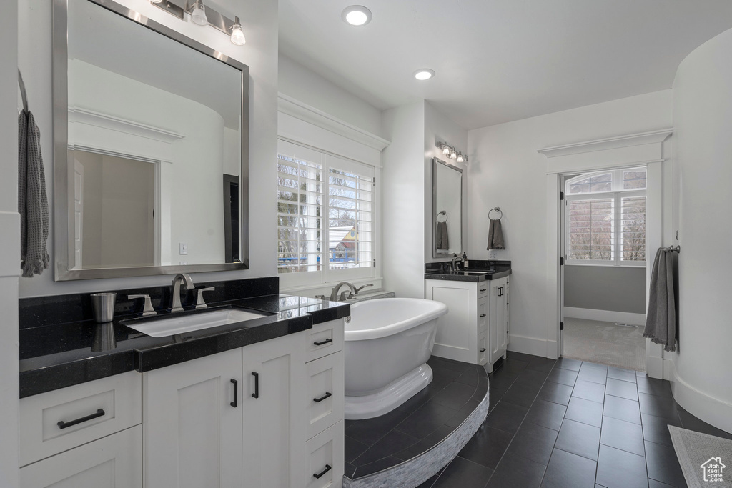Bathroom with tile flooring, a bathtub, oversized vanity, and dual sinks