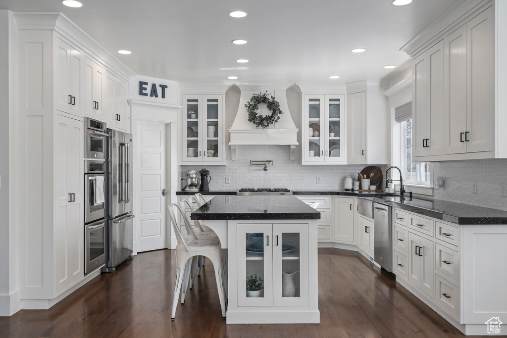 Kitchen featuring white cabinetry, dark hardwood / wood-style flooring, premium range hood, a breakfast bar, and appliances with stainless steel finishes