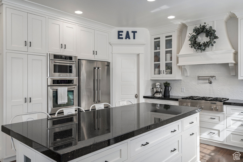 Kitchen featuring dark hardwood / wood-style floors, dark stone countertops, appliances with stainless steel finishes, backsplash, and a kitchen island