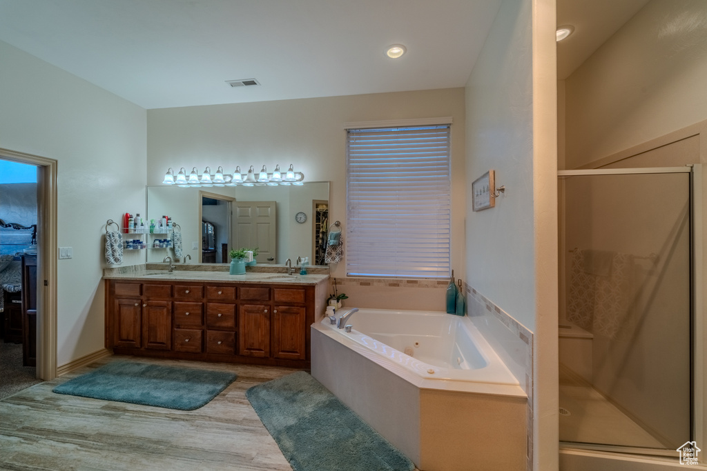Bathroom with wood-type flooring, plus walk in shower, double sink, and vanity with extensive cabinet space