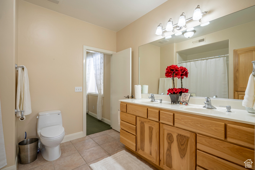 Bathroom with dual sinks, toilet, oversized vanity, and tile floors