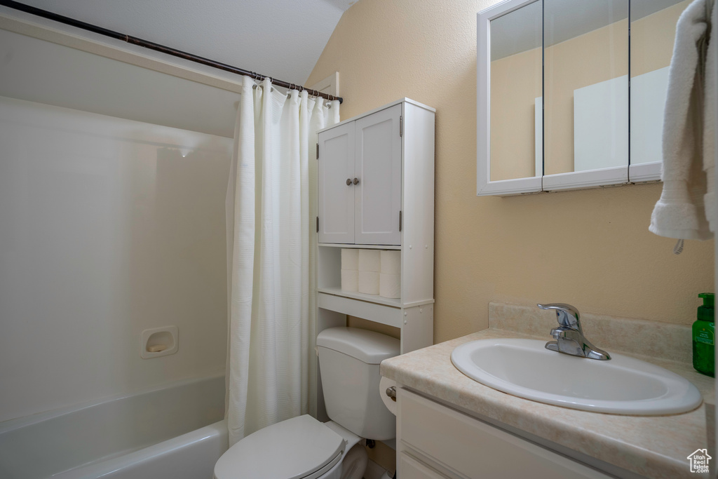 Full bathroom featuring vaulted ceiling, oversized vanity, shower / bath combo with shower curtain, and toilet